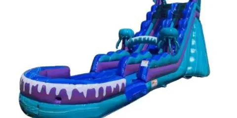 A large, blue and purple inflatable water slide with a shark mouth design at the base.