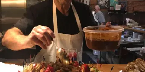 Chef Peter Hadley in a white apron plating a large dish of appetizers in a commercial kitchen.