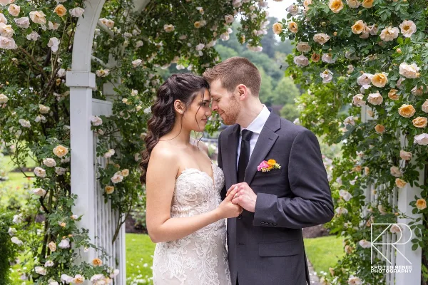 A bride and groom standing together under a floral archway in a garden.
