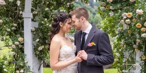 A bride and groom standing together under a floral archway in a garden.