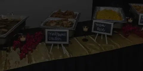 A catering buffet table featuring chafing dishes with fried chicken, yellow rice, and twice-baked potatoes, decorated with red berries and small chalkboard signs.