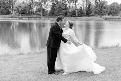 A black and white wedding photograph of a bride and groom dancing by a lake.