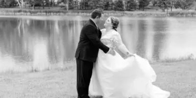 A black and white wedding photograph of a bride and groom dancing by a lake.