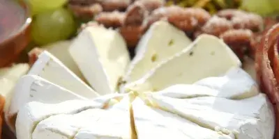 A close-up of a catering spread featuring a wheel of sliced brie cheese, green grapes, and nuts on a wooden board.