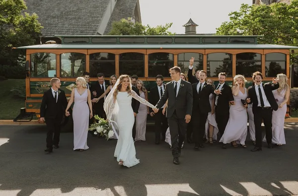 A wedding party walking in front of a trolley charter bus.
