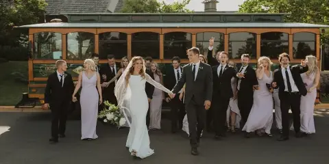 A wedding party walking in front of a trolley charter bus.