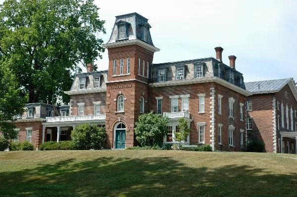 Exterior view of the Oneida Community Mansion House, a historic red brick building with a central tower and white balconies, set on a grassy lawn.