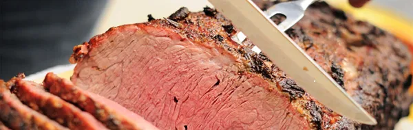 Close-up of sliced smoked brisket with a knife resting on top