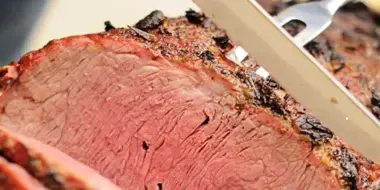 Close-up of sliced smoked brisket with a knife resting on top