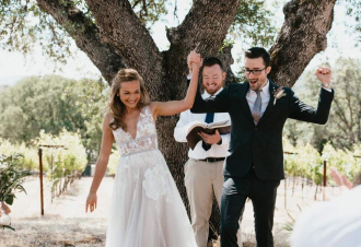 A bride and groom celebrating under a large oak tree in a vineyard setting.