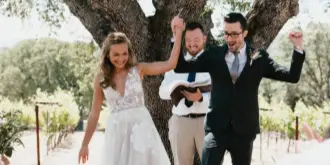 A bride and groom celebrating under a large oak tree in a vineyard setting.