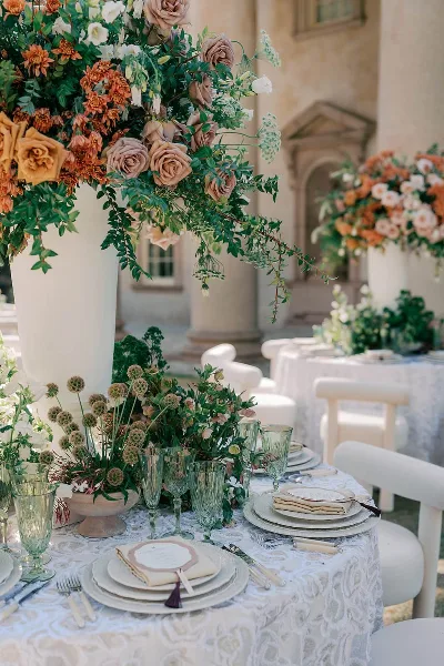 Elegant wedding table setting with lush floral centerpieces, greenery, glassware, and place settings in a classical venue.