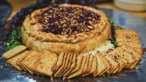 A close-up of a savory tart topped with nuts and berries, served with crackers on a metal platter.