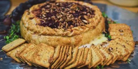 A close-up of a savory tart topped with nuts and berries, served with crackers on a metal platter.