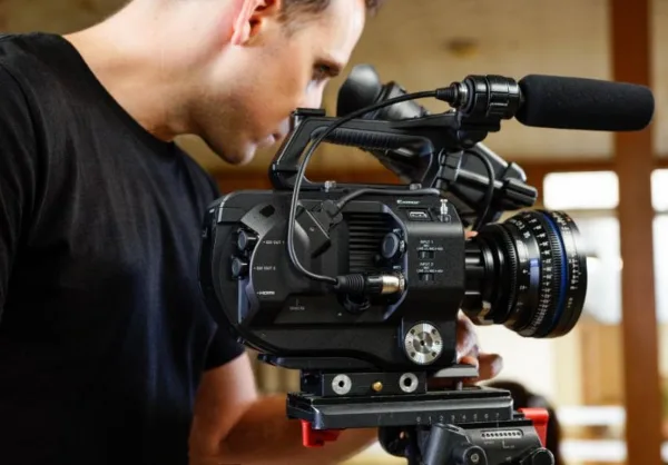 A videographer operating a professional cinema camera with a microphone and lens.