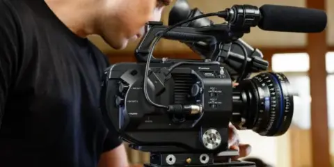 A videographer operating a professional cinema camera with a microphone and lens.