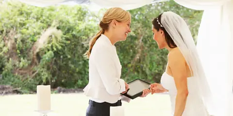 A wedding coordinator in a white shirt smiling and interacting with a bride in a wedding dress and veil.