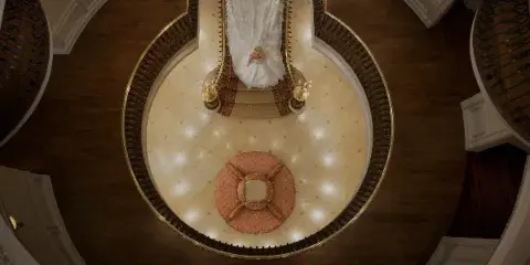 Overhead view of a bride in a white wedding dress standing in a grand, circular architectural atrium with ornate railings and wood flooring.