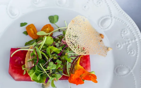 A close-up of a plated gourmet appetizer with microgreens, edible flowers, and a crisp garnish on a white plate.
