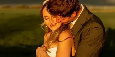 A bride and groom embracing in a field with mountains in the background.