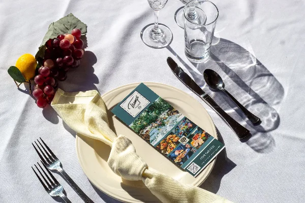 A formally set catering table with a Trumps Catering menu card, silverware, glassware, and a garnish of grapes and a lemon.