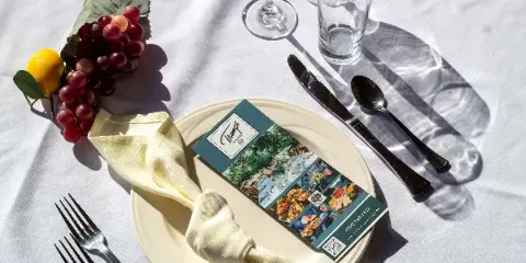 A formally set catering table with a Trumps Catering menu card, silverware, glassware, and a garnish of grapes and a lemon.