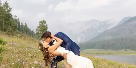 A bride and groom sharing a dip kiss in a wildflower meadow with mountains in the background.