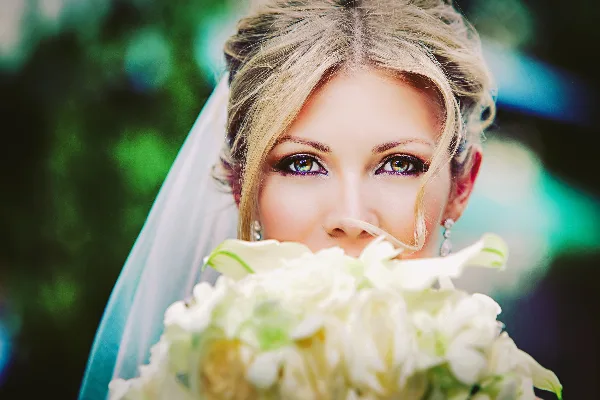 Close-up portrait of a blonde bride wearing a veil and holding a white floral bouquet.