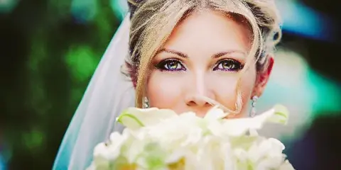 Close-up portrait of a blonde bride wearing a veil and holding a white floral bouquet.