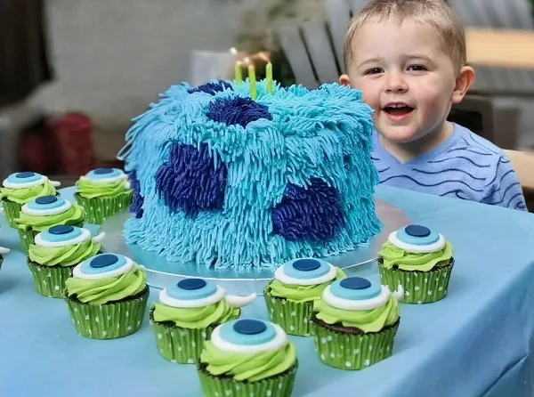 A custom blue and purple textured cake with candles and matching green cupcakes on a table.
