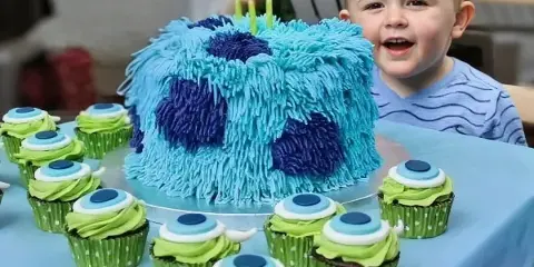 A custom blue and purple textured cake with candles and matching green cupcakes on a table.