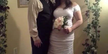 A bride and groom standing together under a floral arch in a wedding dress and suit.