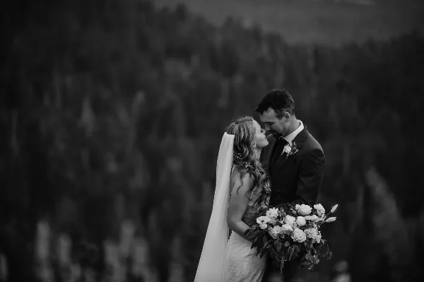 Black and white photograph of a bride and groom embracing outdoors with a bouquet of flowers.