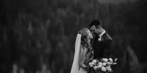 Black and white photograph of a bride and groom embracing outdoors with a bouquet of flowers.