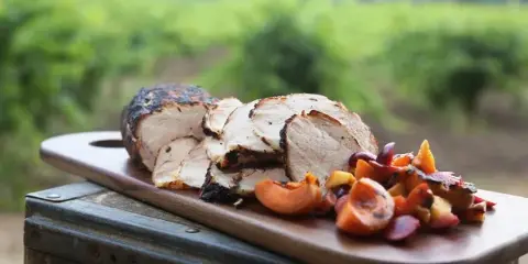 A plated dish of sliced roasted meat and roasted vegetables served on a wooden board in a vineyard setting.