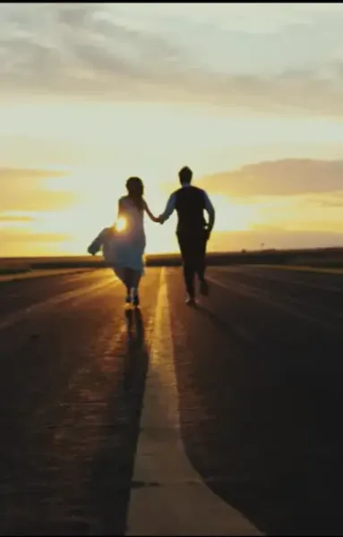 A wedding couple running hand-in-hand down a road at sunset.
