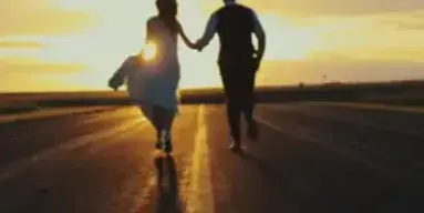 A wedding couple running hand-in-hand down a road at sunset.