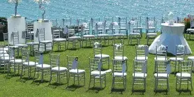 Waterside wedding ceremony setup with white chairs, cocktail tables, and a blue ocean backdrop.