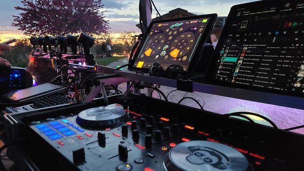 A professional DJ booth featuring turntables, a mixer, and lighting equipment set up at an outdoor event.