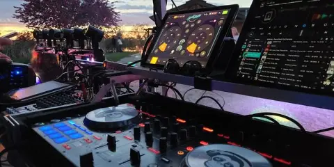 A professional DJ booth featuring turntables, a mixer, and lighting equipment set up at an outdoor event.