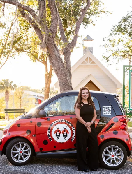 A woman in a black dress standing next to a red Smart car with 'Ladybug Mobile Notary Services' branding and a ladybug logo.