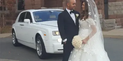 A bride and groom standing next to a white Rolls-Royce limousine.