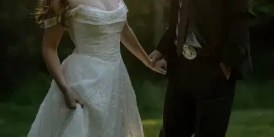 A bride and groom holding hands and smiling at each other in a sunlit outdoor setting.