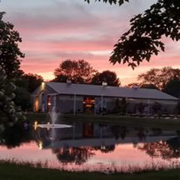 A large barn-style wedding venue building reflected in a pond at sunset.