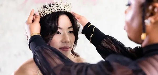 A hair and makeup artist placing a tiara on a bride's head.