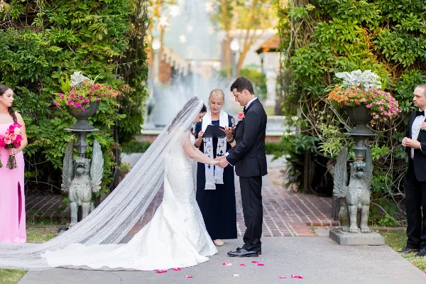 A bride and groom exchanging vows with an officiant in a garden setting.