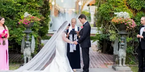 A bride and groom exchanging vows with an officiant in a garden setting.