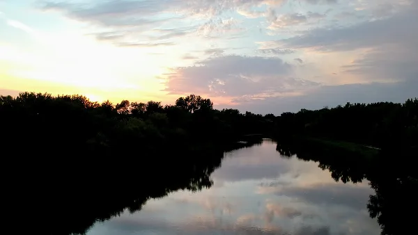 A calm river reflecting a sunset sky, bordered by dark silhouettes of trees and vegetation.