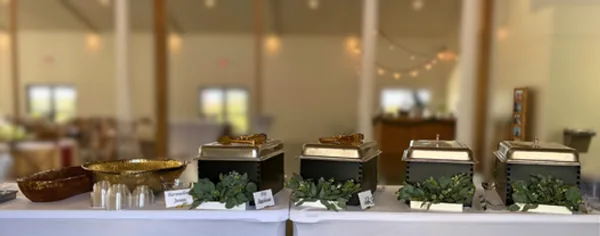 A catering buffet table featuring multiple chafing dishes and serving bowls set up in an event venue.