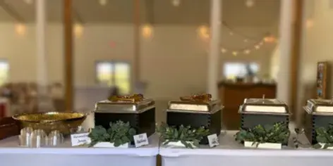 A catering buffet table featuring multiple chafing dishes and serving bowls set up in an event venue.